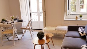 Ett mysigt vardagsrum med en soffa, ett litet bord, en stol och en matplats med ett bord och stolar.