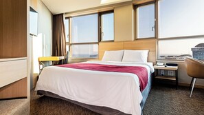 A hotel room with a bed, a desk, a chair, and a view of the city. - Shin Shin Hotel Jeju Eastern (Seogwipo)