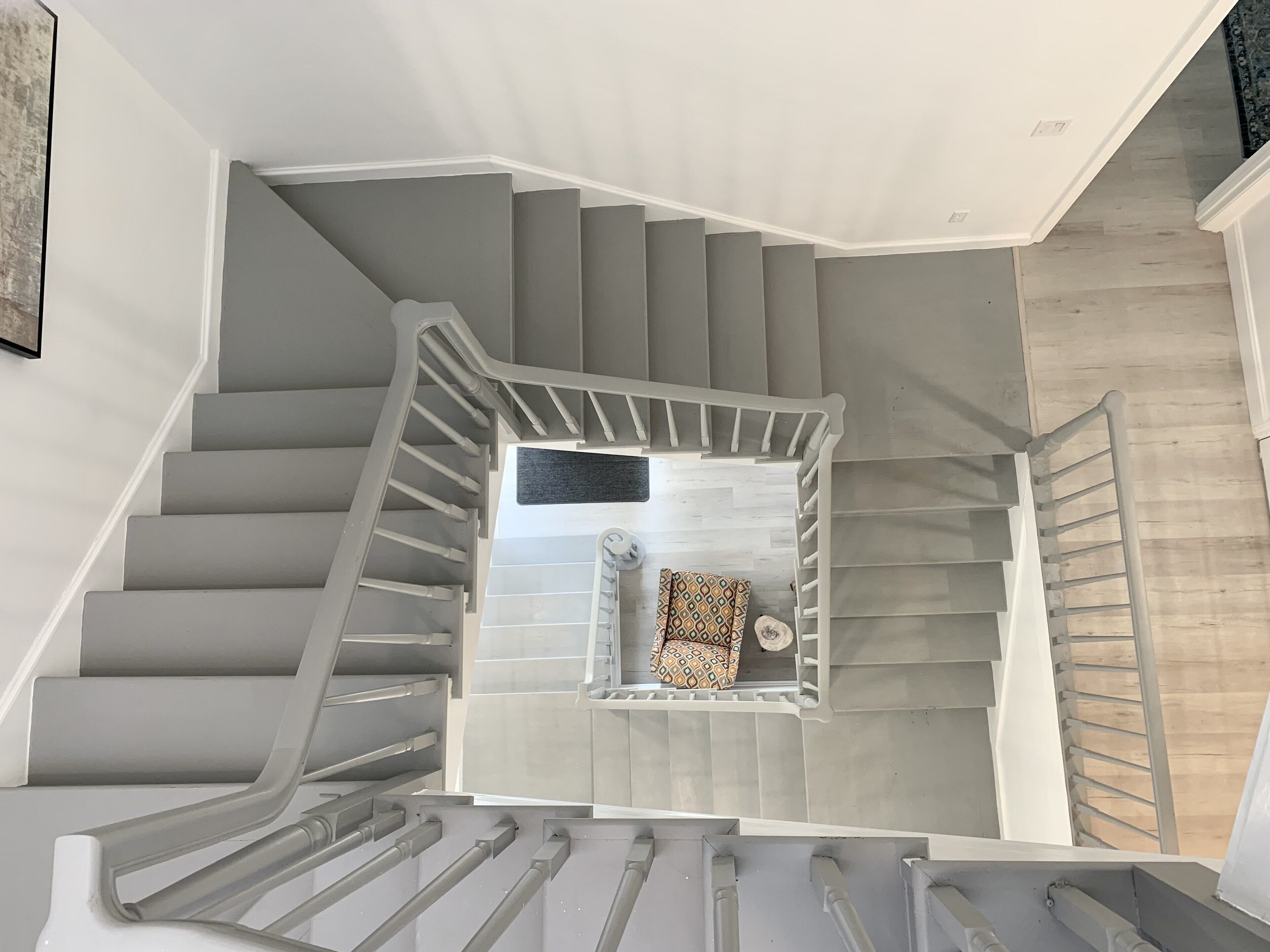 Eine moderne Treppe mit Geländer, die zu einer Empfangsebene mit einem gemusterten Teppich und einer kleinen Sitzecke führt.