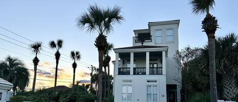 A two-story building with a balcony, surrounded by palm trees, and a driveway leading to the entrance.