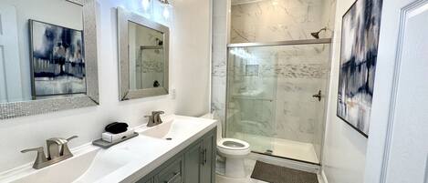 A modern bathroom with two sinks, a glass shower enclosure, and a toilet.