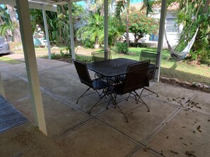 Eine Terrass mit Tisch und Stühlen, umgeben von Pflanzen und einer Hängematte.