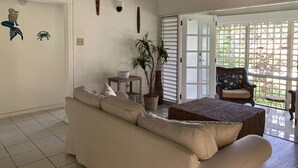 Ett rymligt vardagsrum med en beige soffa, en rottingpall, ett litet bord med en korg och en krukväxt.