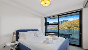 Un dormitorio con una cama grande, una mesita de noche y vistas a un lago y montañas.