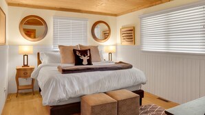 A bedroom with a wooden ceiling, two bedside tables with lamps, a bed with white bedding, a deer pillow, and a bench. - The Kind of Place You Stop Rushing the Moment You Arrive | Bungalow on Crowe (Highlands)