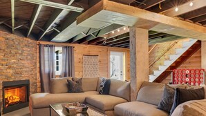 A cozy living room with a brick wall, a fireplace, a sectional sofa, and a glass coffee table. - The Kind of Place You Stop Rushing the Moment You Arrive | Bungalow on Crowe (Highlands)
