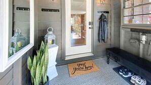 A modern entryway with a white door, a welcome mat, a potted plant, and a coat rack. - The Kind of Place You Stop Rushing the Moment You Arrive | Bungalow on Crowe (Highlands)
