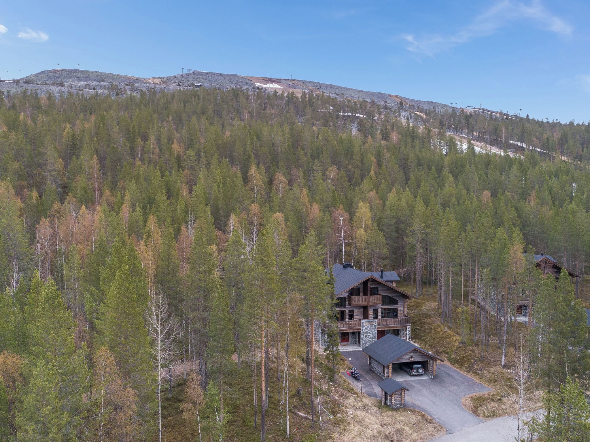A cabin with a stone exterior, multiple decks, and a driveway leading to a garage.