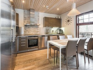 A modern kitchen with a built-in oven, a dining area with a white table and chairs, and a large window with a view.