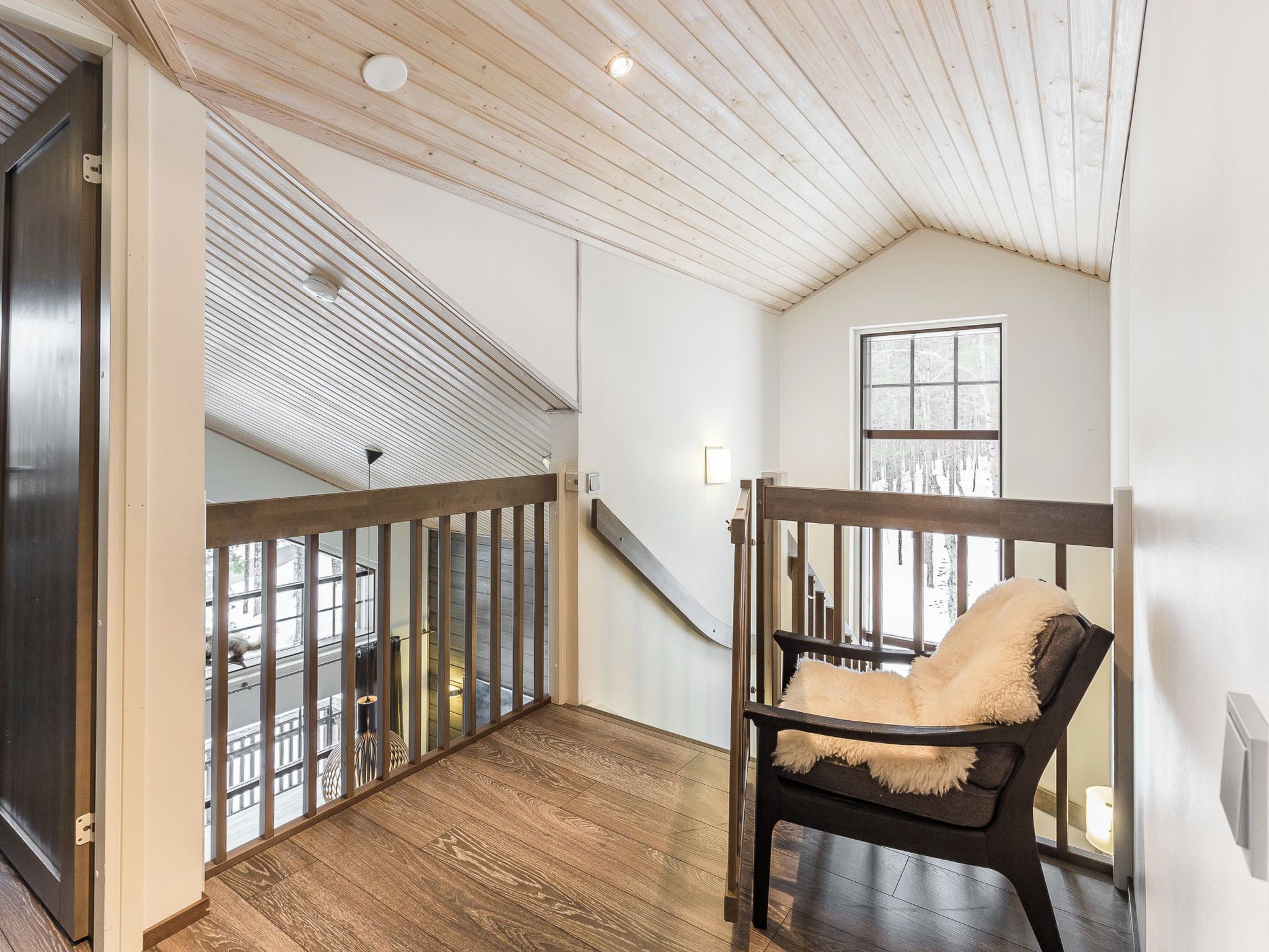 Una habitación amplia con techo alto, piso de madera, vista a un paisaje nevado por la ventana y un sillón acogedor con un plaid de piel.