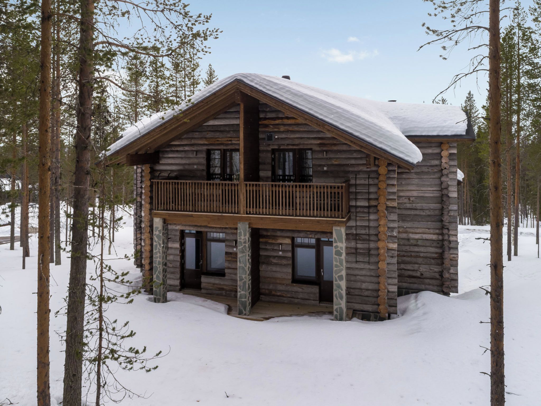 Une cabane en rondins dotée d’un balcon, entourée de neige et d’arbres.
