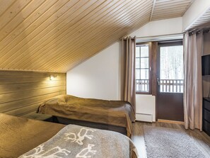A room with two beds, a wooden sloped ceiling, a window with curtains, and a radiator.
