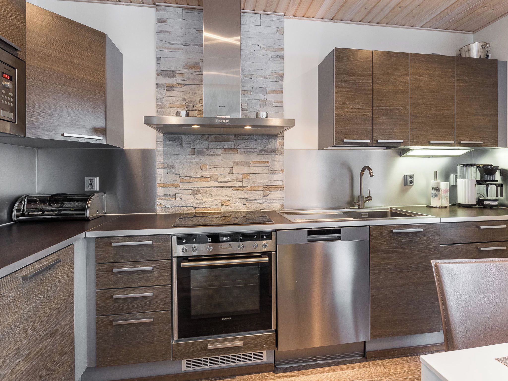 Une cuisine moderne dotée d’appareils électroménagers intégrés, d’un pare-feu en pierre et de meubles de rangement en bois.