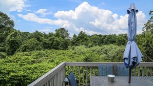 Una terraza con mesa y sillas, una sombrilla y vistas a abundante vegetación bajo un cielo parcialmente nublado.