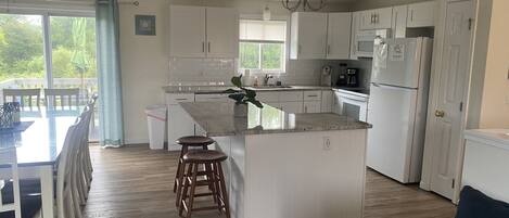 A modern kitchen with white cabinets, a central island, and a dining area with a table and chairs.