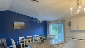 Una cocina moderna con armarios blancos, encimera de granito y zona de comedor con sillas blancas.