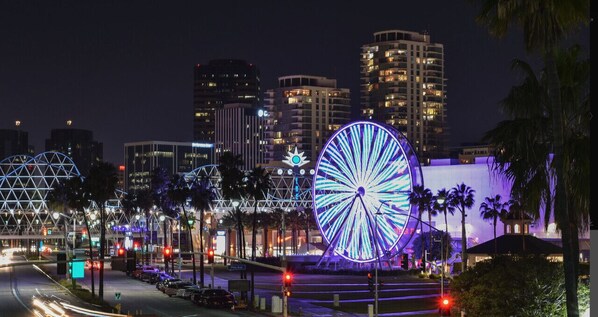 A cityscape at night with a prominent illuminated Ferris wheel and modern buildings in the background.