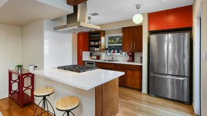 Een moderne keuken met een centraal eiland, houten kasten, een roestvrijstalen koelkast en een rode barstoel.