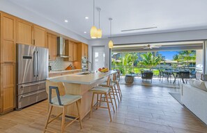A modern kitchen with a large island, stainless steel appliances, and a view of a tropical landscape.