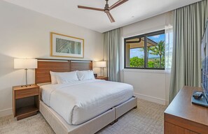 Ein Hotelzimmer mit einem großen Bett, zwei Nachttischen, einem Deckenventilator, einem Fenster mit Blick ins Grüne und einem gerahmten Bild an der Wand.