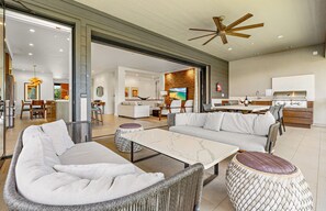 A spacious living area with a sofa, coffee table, and ottoman, a kitchen with a grill, and a dining area with chairs and a table.