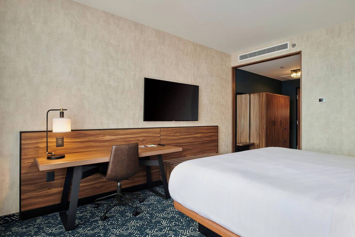 Ein Hotelzimmer mit einem Bett, einem Schreibtisch mit Stuhl, einem Fernseher und einem Kleiderschrank.