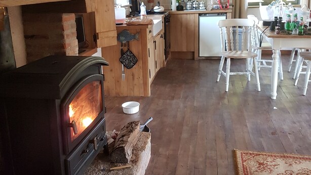 A rustic kitchen with a wood-burning stove, wooden cabinets, and a dining area with white chairs. - Charming 1-Bed Cottage in The Hideout (La chapelle montbrandeix)