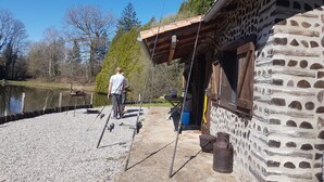 A rustic stone building with a wooden porch, fishing rods, and a fishing rod holder. - Charming 1-Bed Cottage in The Hideout (La chapelle montbrandeix)