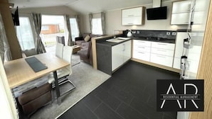A modern kitchen with a dining area, a sofa, and a TV mounted on the wall. - Luxury 3 bed mobile home on the sea (Southampton)