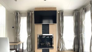 Ein modernes Wohnzimmer mit flachbildfernseher an einer Holzwand, darunter ein Kamin und eine Sitzecke mit Sofa und Sessel.