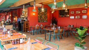 A restaurant with wooden tables and chairs, a kitchen area, and a colorful mural on the wall. - 1 Bed Shepherds Hut - Sleeps 2 -Wood Fired Hot Tub (Charlton musgrove)