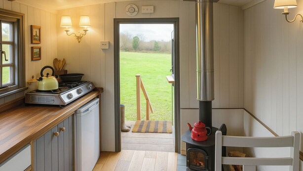 A cozy kitchen with a stove, kettle, and a view of a grassy yard. - 1 Bed Shepherds Hut - Sleeps 2 -Wood Fired Hot Tub (Charlton musgrove)