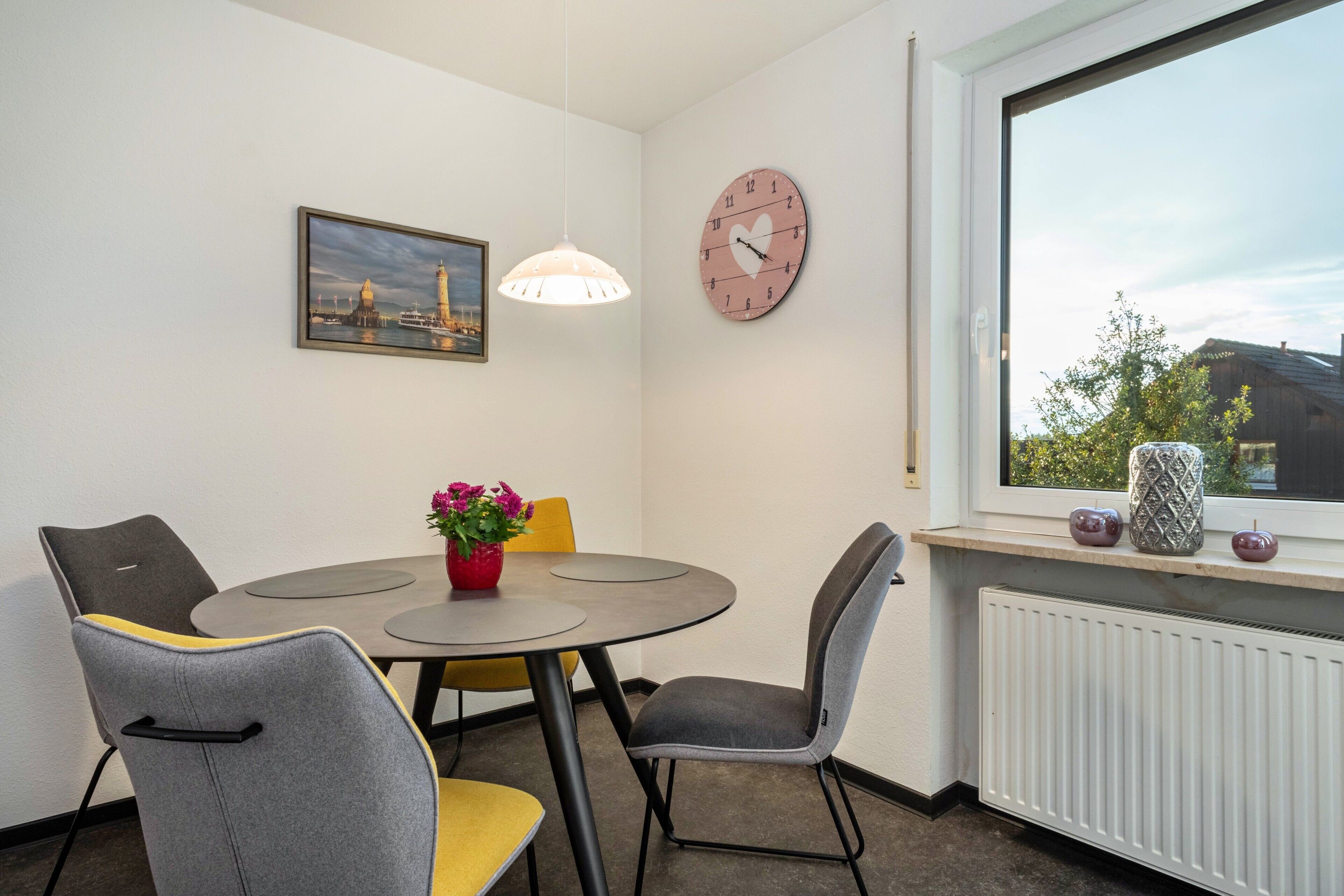Ein Essbereich mit rundem Tisch, zwei Stühlen, einer Uhr, einer Pendelleuchte und einem Fenster mit Blick.