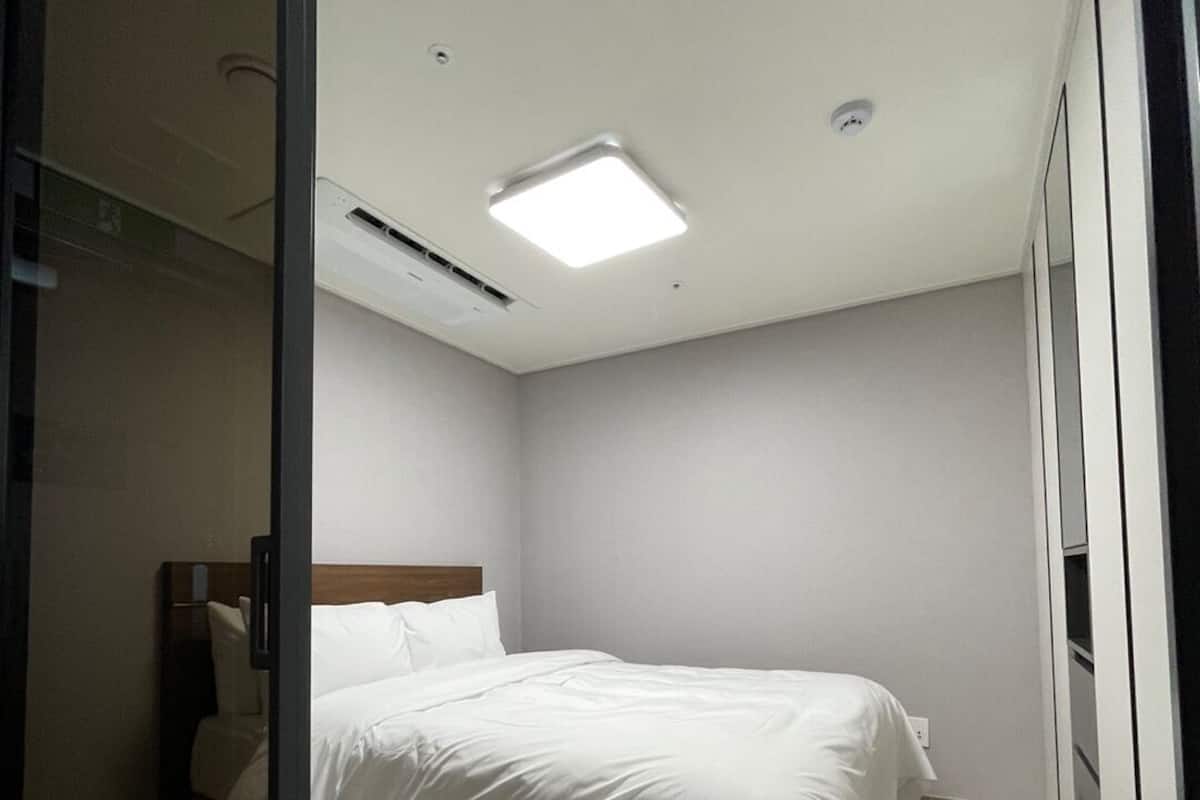 Une chambre d’hôtel avec un lit simple, une tête de lit en bois, une table de chevet et une grande fenêtre.