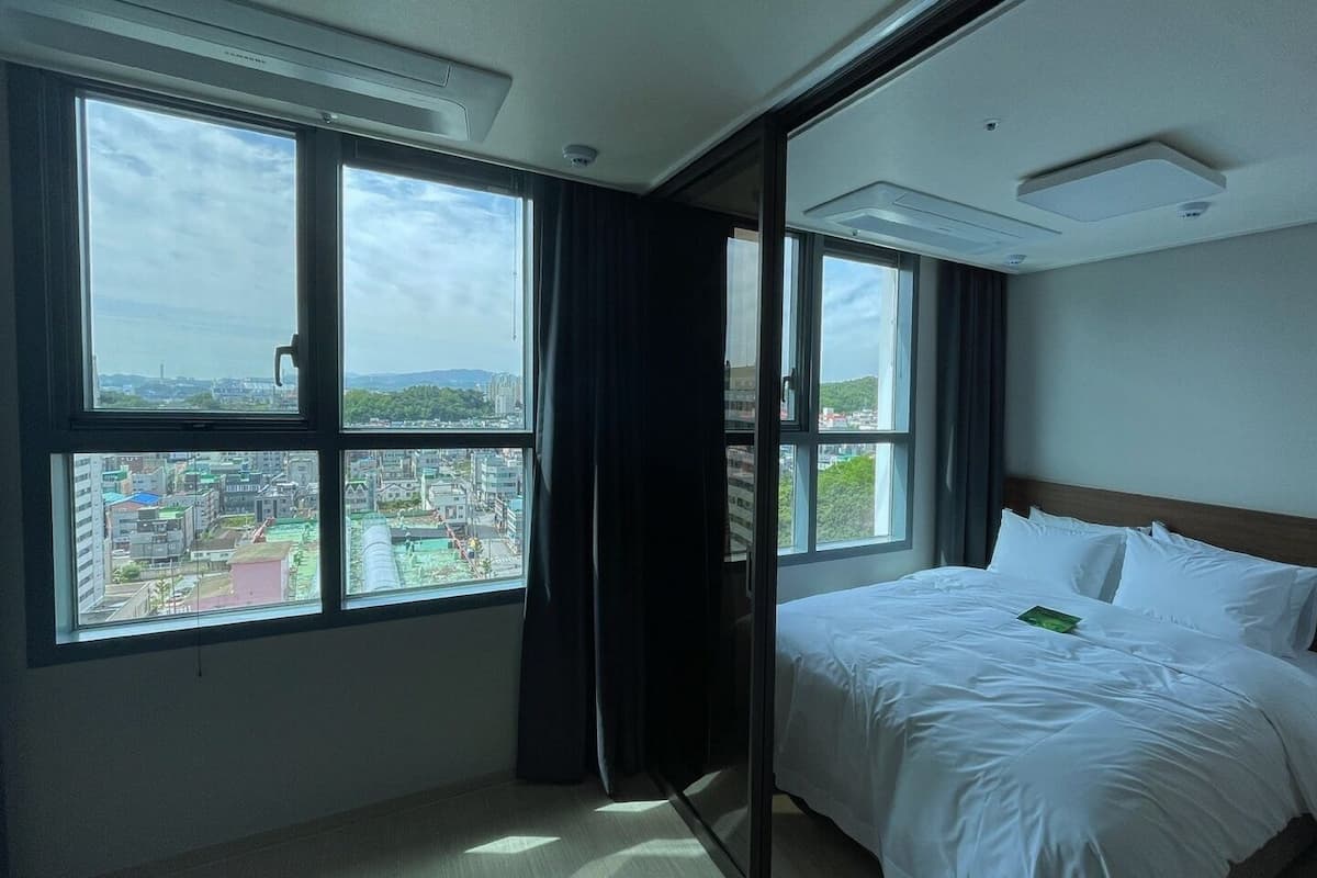 Une chambre d’hôtel avec un lit, une fenêtre donnant sur la ville et un rideau.