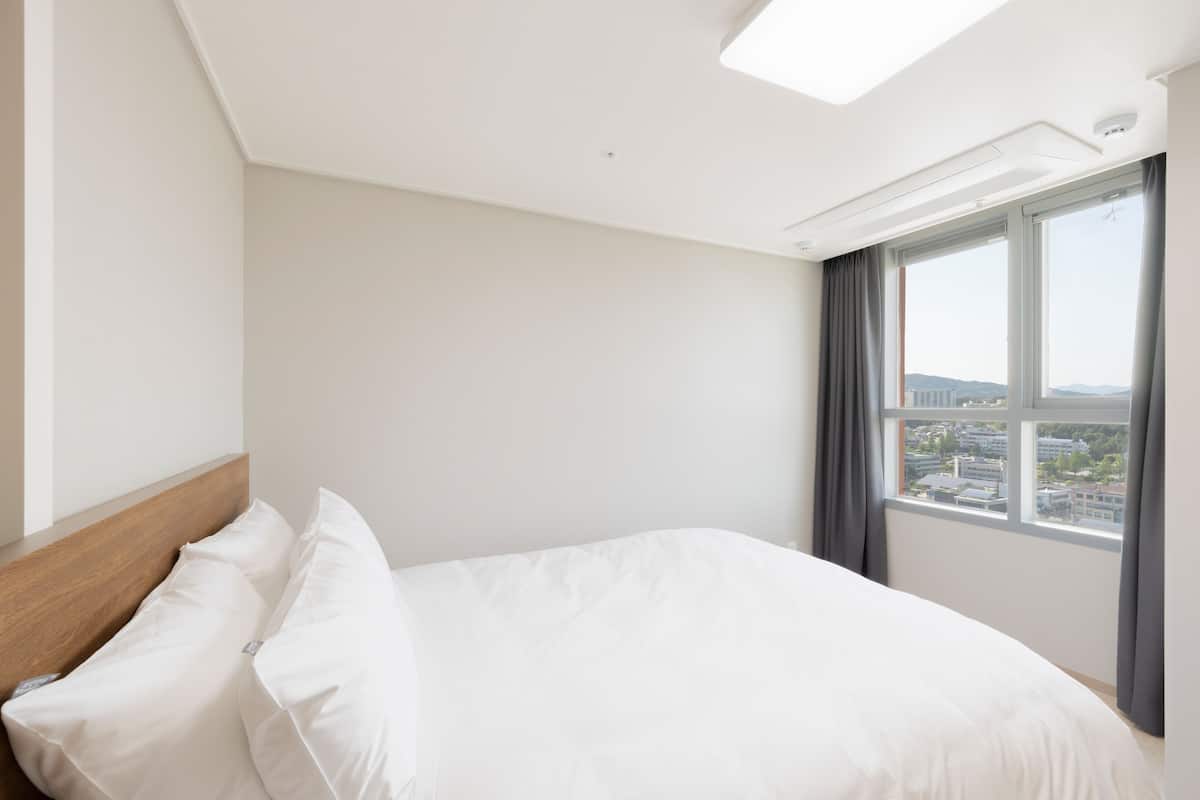 Une chambre d’hôtel avec un grand lit, une tête de lit en bois, une fenêtre donnant sur la ville et une lucarne.