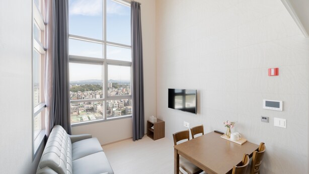 A modern living room with a large window, a sofa, a dining table with chairs, a flat-screen TV, and a small side table. - Donghae Oceancity Residence Hotel (Donghae)