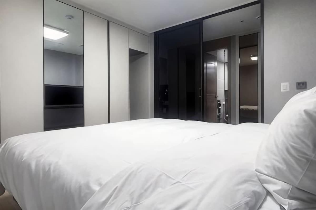 A hotel room with a large bed, a wardrobe, a mirror, and a door leading to a bathroom.