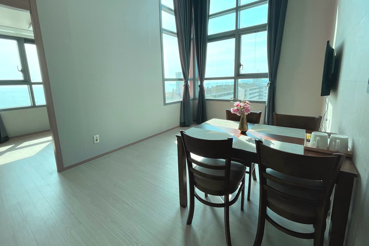 Une pièce spacieuse avec une grande fenêtre, une table à manger avec des chaises et un vase rempli de fleurs.