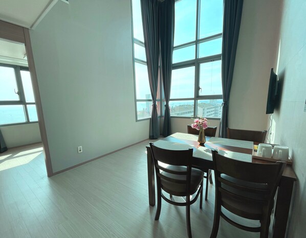 A spacious room with a large window, a dining table with chairs, and a vase with flowers. - Donghae Oceancity Residence Hotel (Donghae)