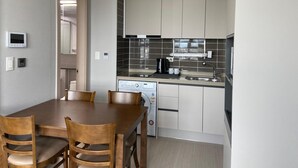 A modern kitchen with white cabinets, a black tiled backsplash, and a built-in oven. There is a dining table with four chairs and a coffee maker on the counter. - Donghae Oceancity Residence Hotel (Donghae)