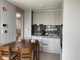 Una cocina moderna con armarios blancos, un salpicadero de azulejos negros y un horno empotrado. Hay una mesa de comedor con cuatro sillas y una cafetera en la encimera.