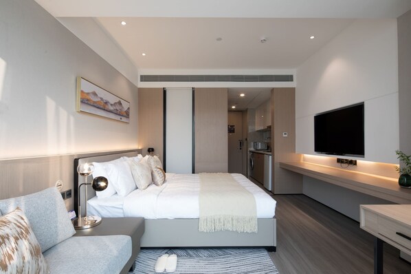 Una habitación de hotel moderna con una cama, una mesita de noche, un televisor, un sofá y una zona de cocina.