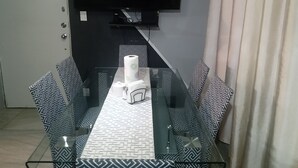 Ein moderner Essbereich mit Glastisch und gemusterten Stühlen, einem an der Wand befestigten Flachbildfernseher und einem Teppich mit Muster.