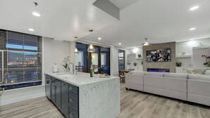 A modern kitchen with a marble island, a dining area with a sofa, and a TV mounted on the wall.