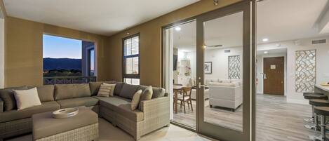 A modern living room with a sectional sofa, a small ottoman, and a dining area with a table and chairs.