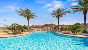 A clear blue pool surrounded by palm trees and lounge chairs, with a mountainous backdrop.