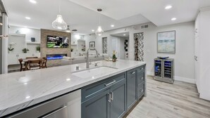 A modern kitchen with a marble countertop, grey cabinets, and a built-in wine cooler.