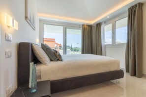 A modern bedroom with a large bed, a nightstand, a vase, and a view of the outside.