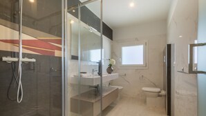 Un bagno moderno con cabina doccia in vetro, lavandino bianco, servizi igienici e pavimento in marmo.
